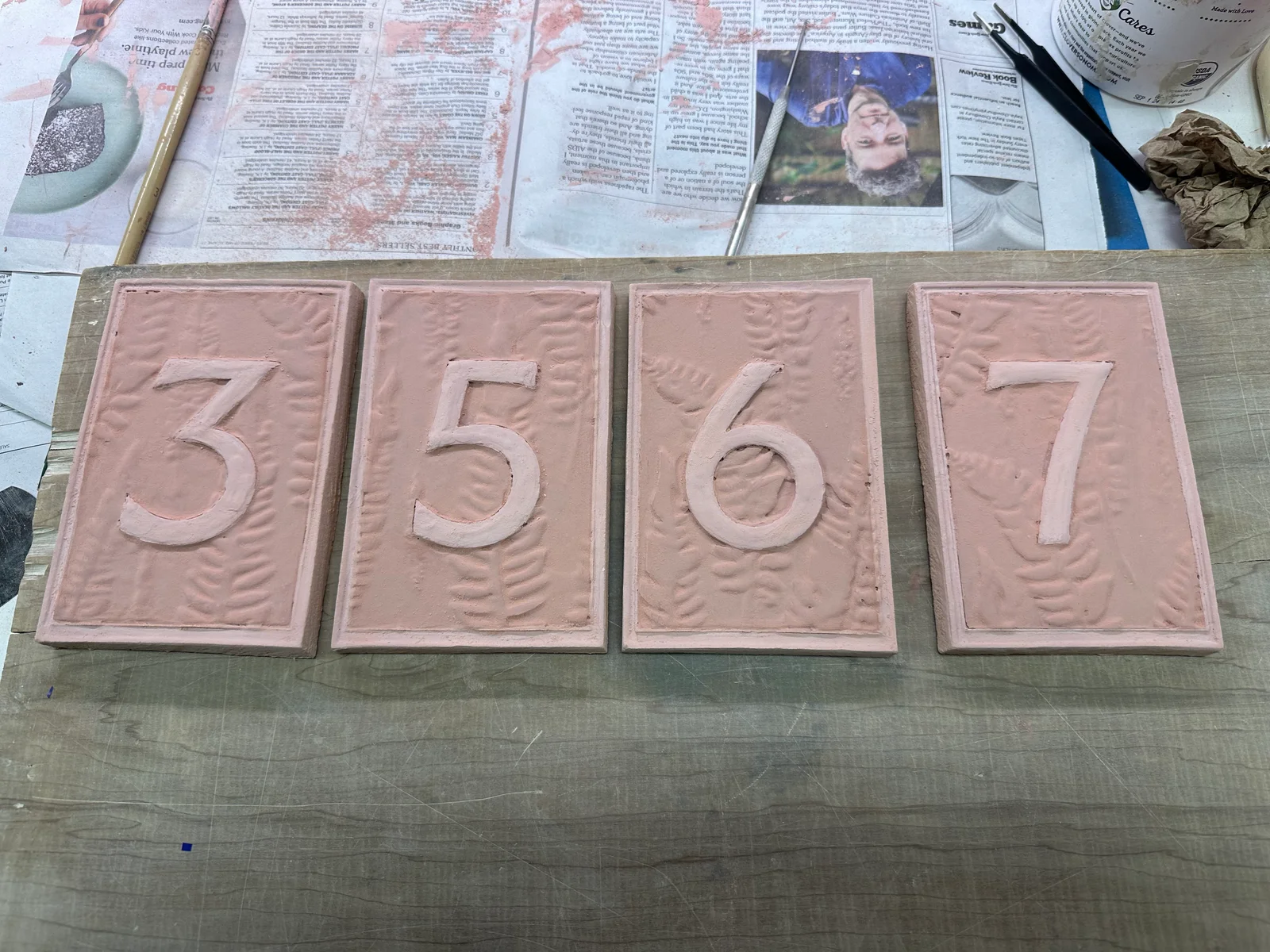 Four raised-fern number tiles, 3, 5, 6 and 7, laid out before firing